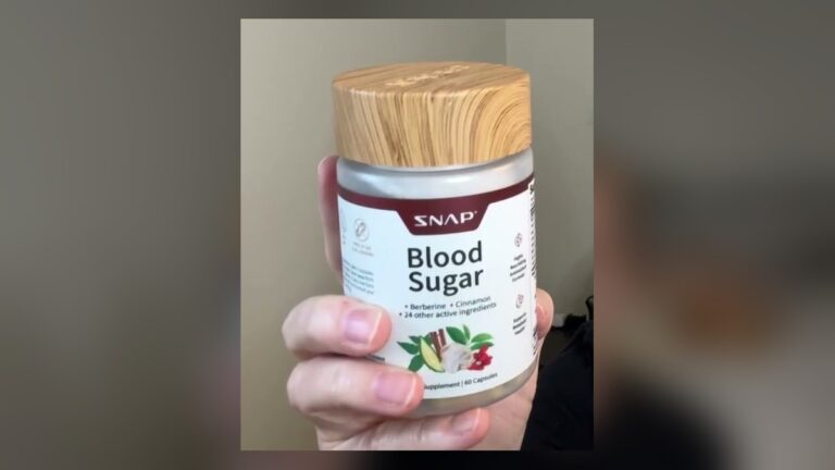 Hand holding a Snap Blood Sugar supplement bottle with a wood-look lid and a white label listing berberine, cinnamon and 24 other active ingredients