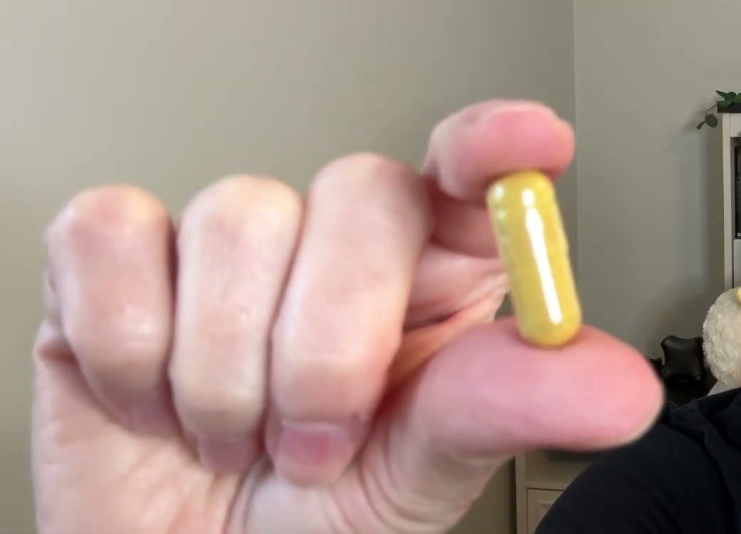 Fingers holding up one clear Snap Blood Sugar Blend capsule filled with yellow powder