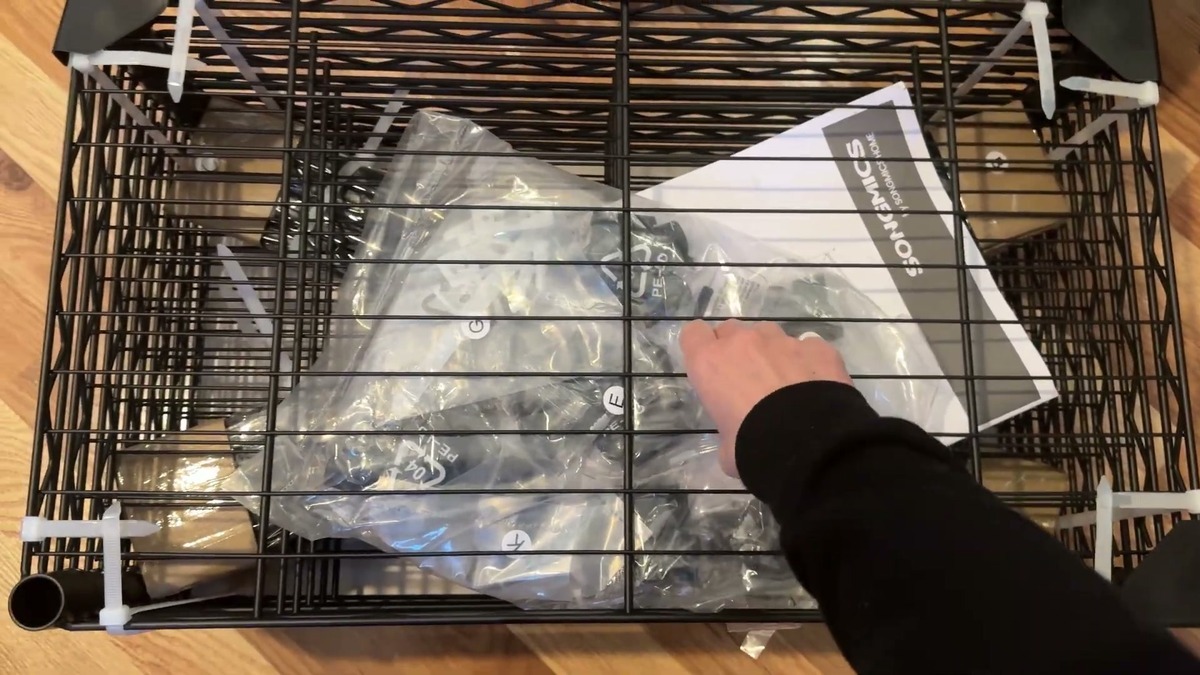 SONGMICS wire shelf frame lifted out of its box in one piece, with bagged parts and the instruction booklet inside