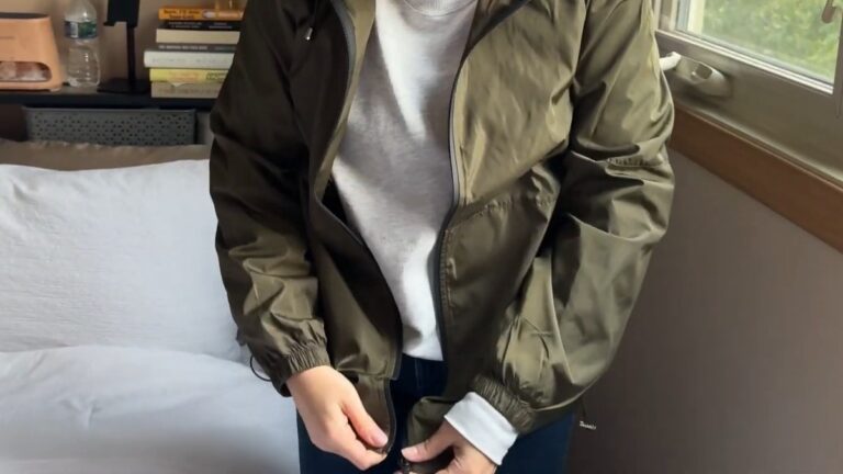 Army green TCOT packable rain jacket worn open over a gray crewneck sweatshirt, with elastic cuffs and a black front zipper