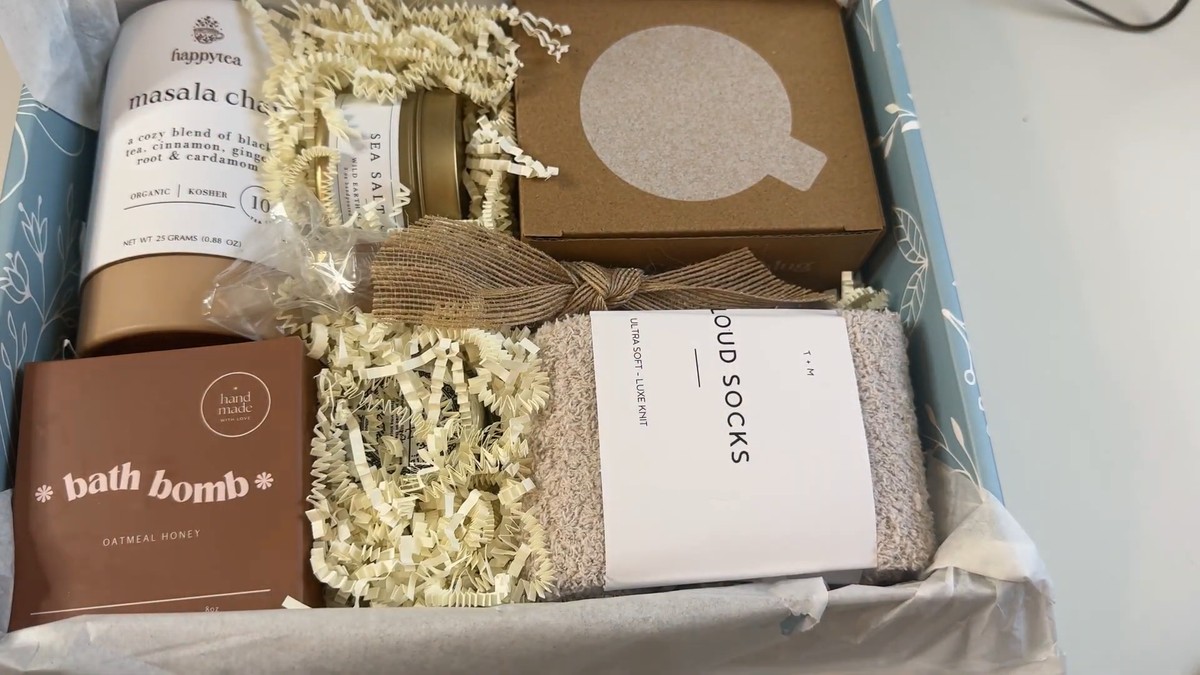 Open Unboxme gift box packed snugly with a happytea masala chai tin, a sea salt and sage candle, a boxed mug, an oatmeal honey bath bomb and a pair of cloud socks in cream crinkle paper.
