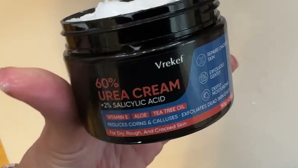 Hand holding a black tub of VREKEF 60% Urea Cream with 2% salicylic acid, label listing vitamin E, aloe and tea tree oil
