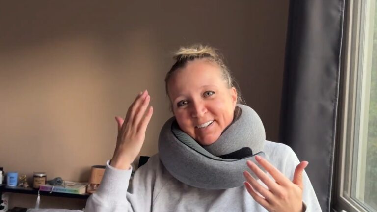 Smiling woman wearing the gray WEERSHUN travel pillow wrapped snugly around her neck over a light gray sweatshirt