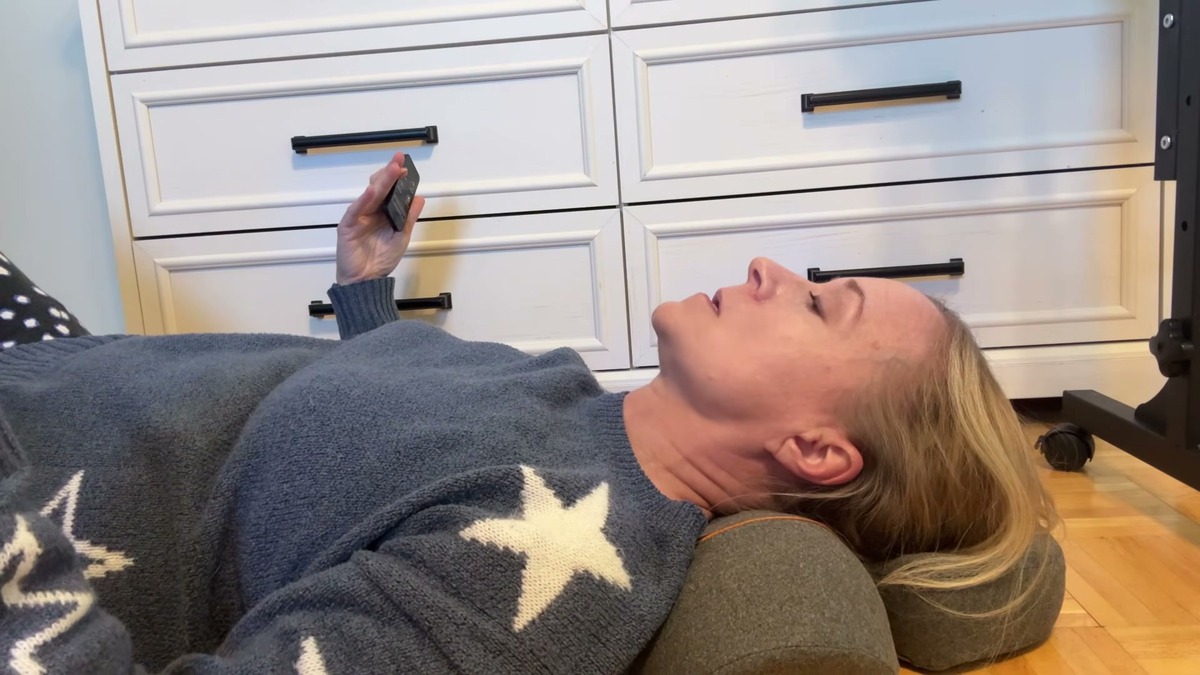 Jen lying on the floor with the Zenvita neck massage pillow under her neck, holding the remote