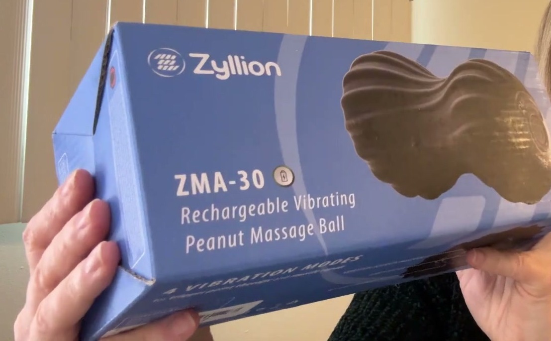 Blue Zyllion ZMA-30 Rechargeable Vibrating Peanut Massage Ball box held in two hands, with 4 vibration modes printed along the bottom edge